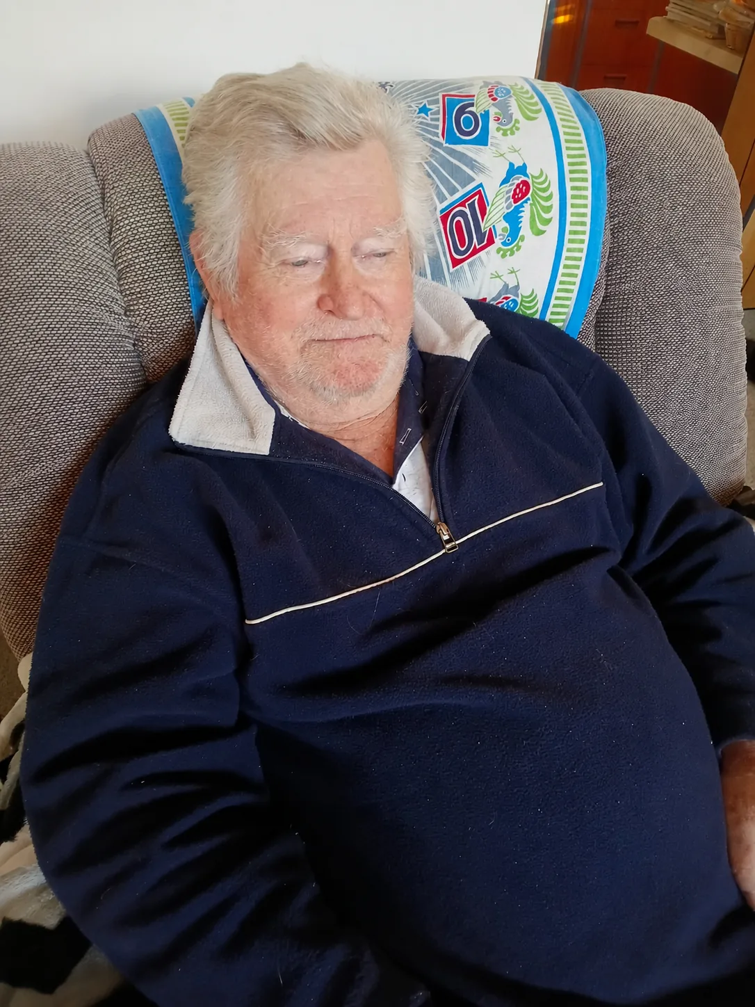 Jim relaxing in an armchair, eyes closed, wearing a navy quarter-zip top