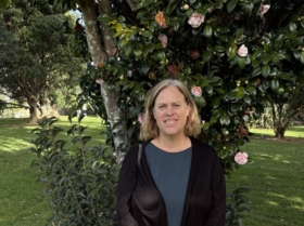Carolyn McCutcheon smiling in a garden in front of a flowering camellia tree