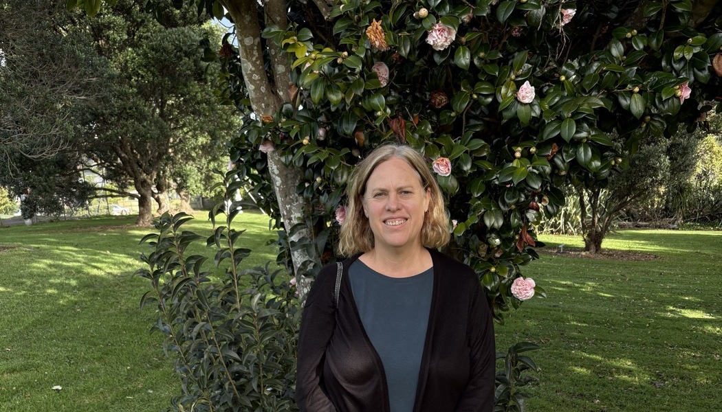 Carolyn McCutcheon smiling in a garden in front of a flowering camellia tree