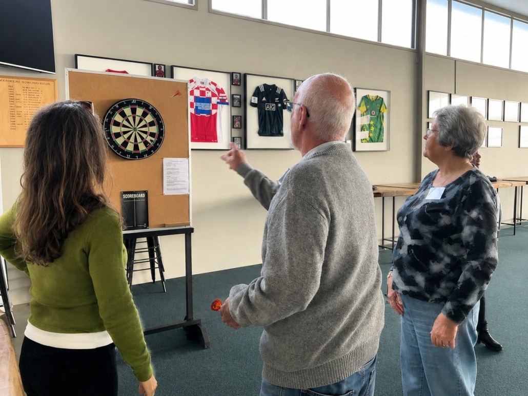 Sporting Memories Kerikeri – darts and sporting memorabilia Sporting Memories Kerikeri members playing darts beside a display of framed sports jerseys